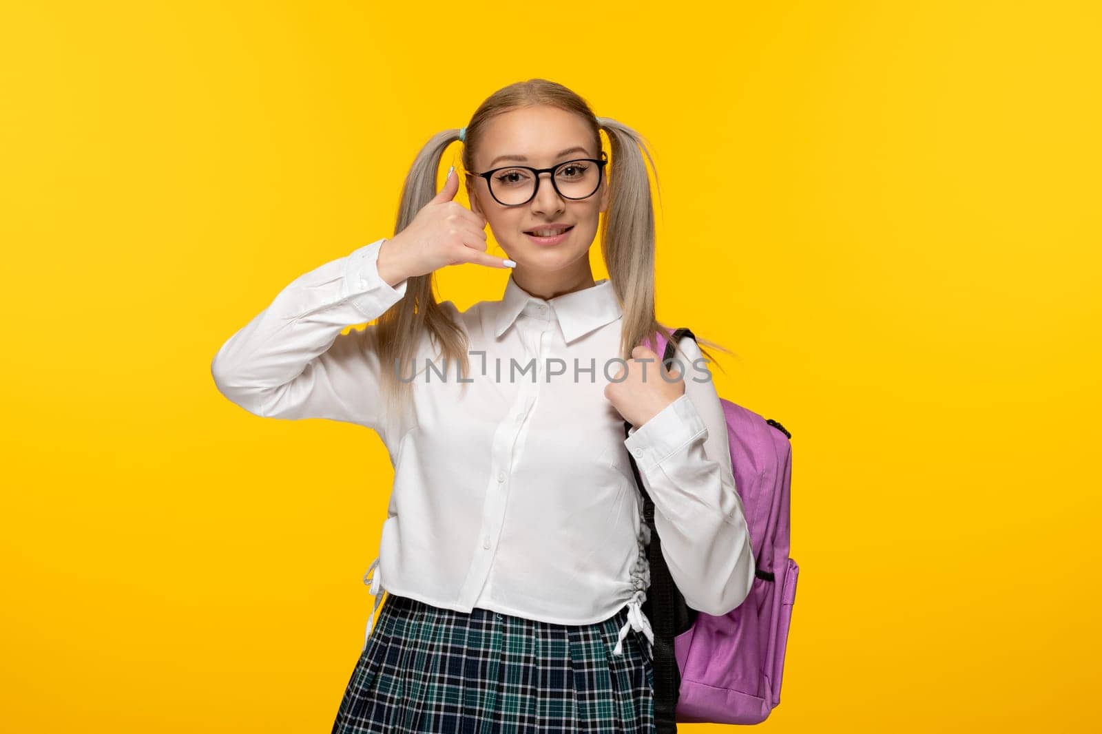 world book day blonde happy schoolgirl in uniform on yellow background showing calling gesture sign