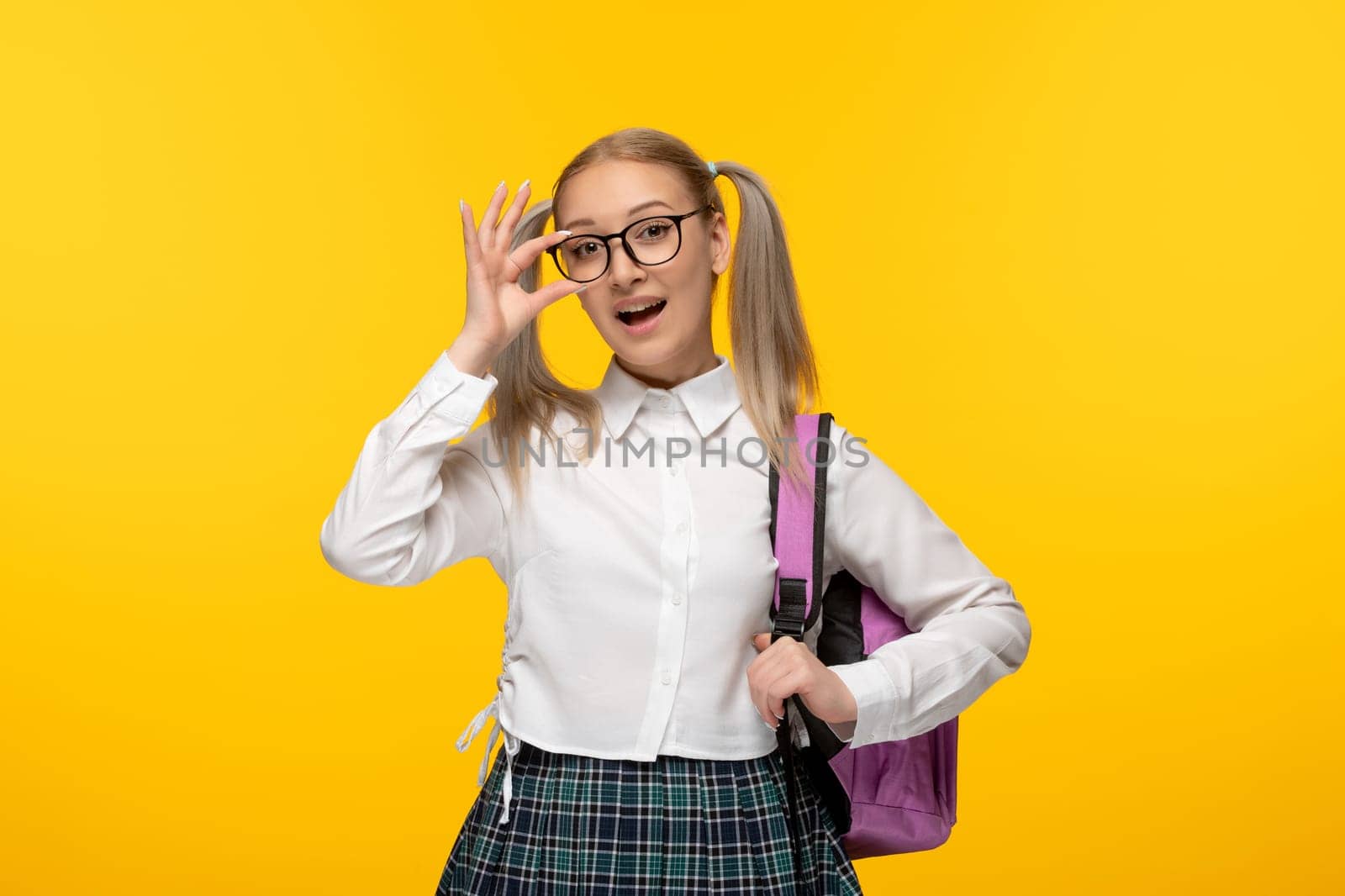 world book day blonde schoolgirl with ponytails and pink backpack touching glasses