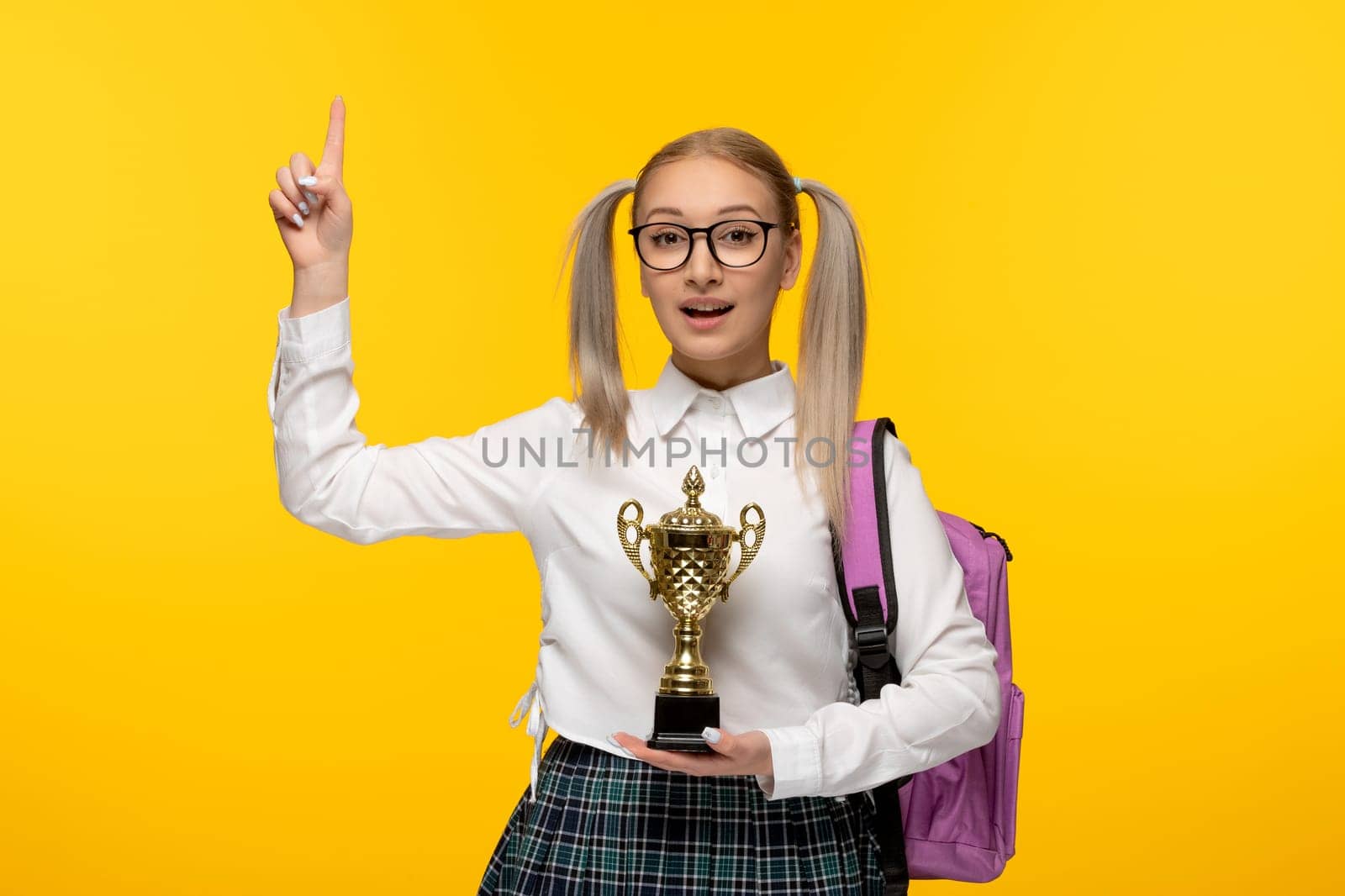 world book day excited school girl with pony tails holding trophy on yellow background