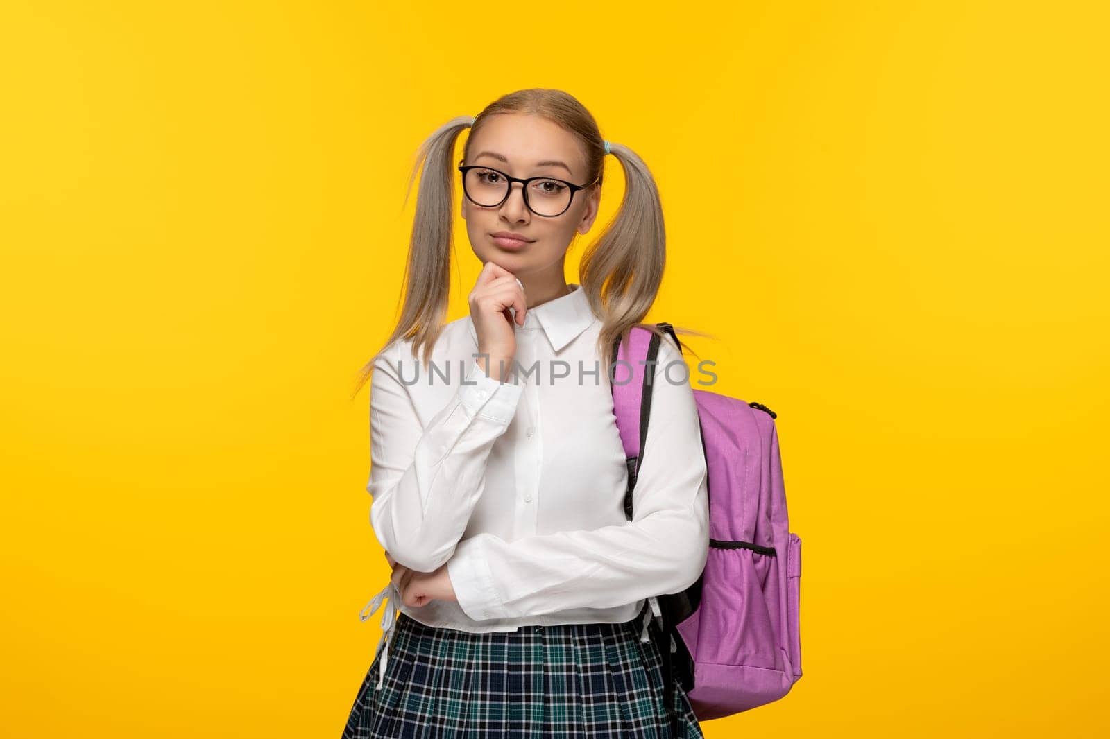 world book day serious schoolgirl in glasses and pink backpack on yellow background