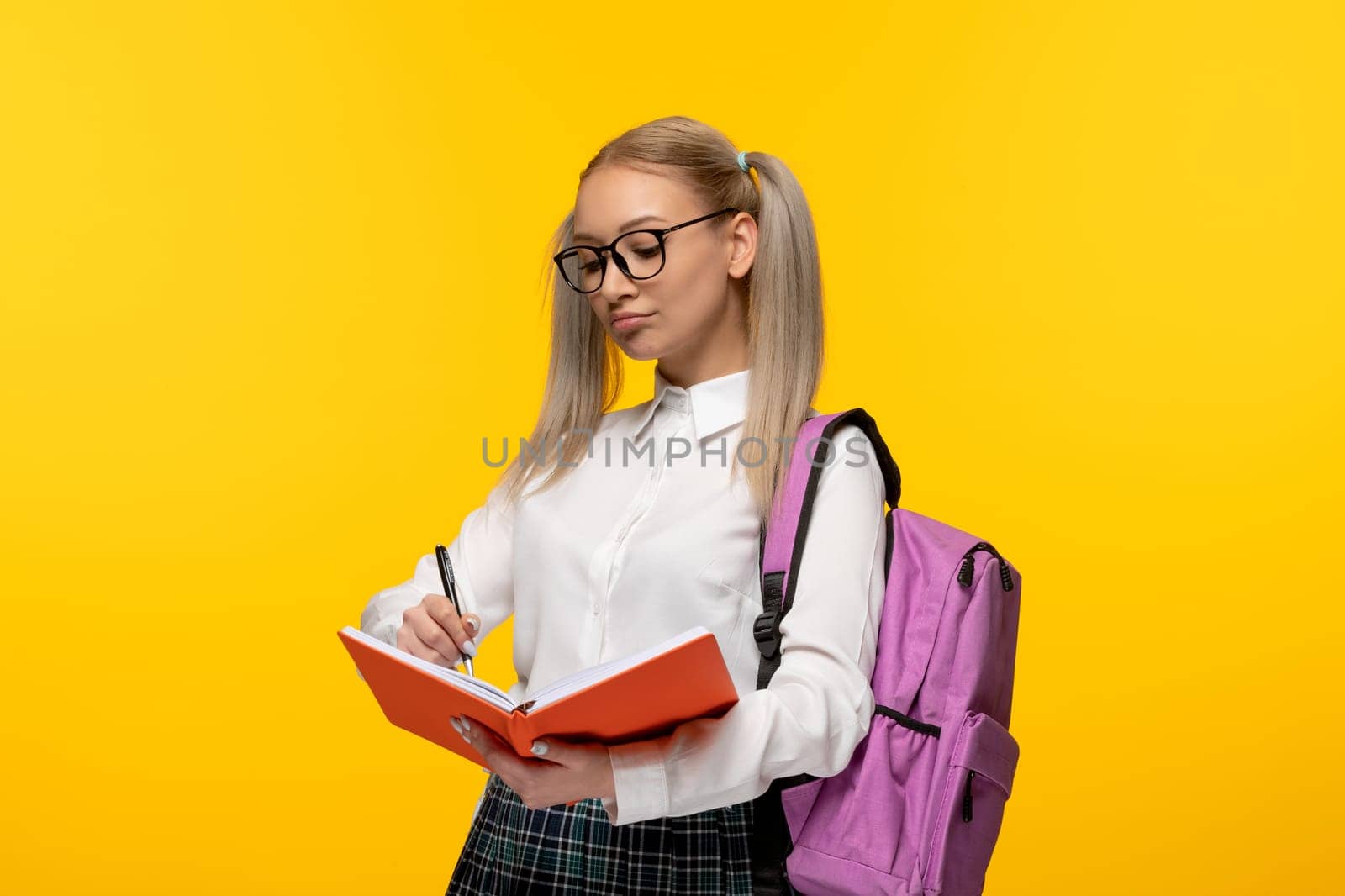 world book day smart schoolgirl with pony tails writing in the notebook on yellow background