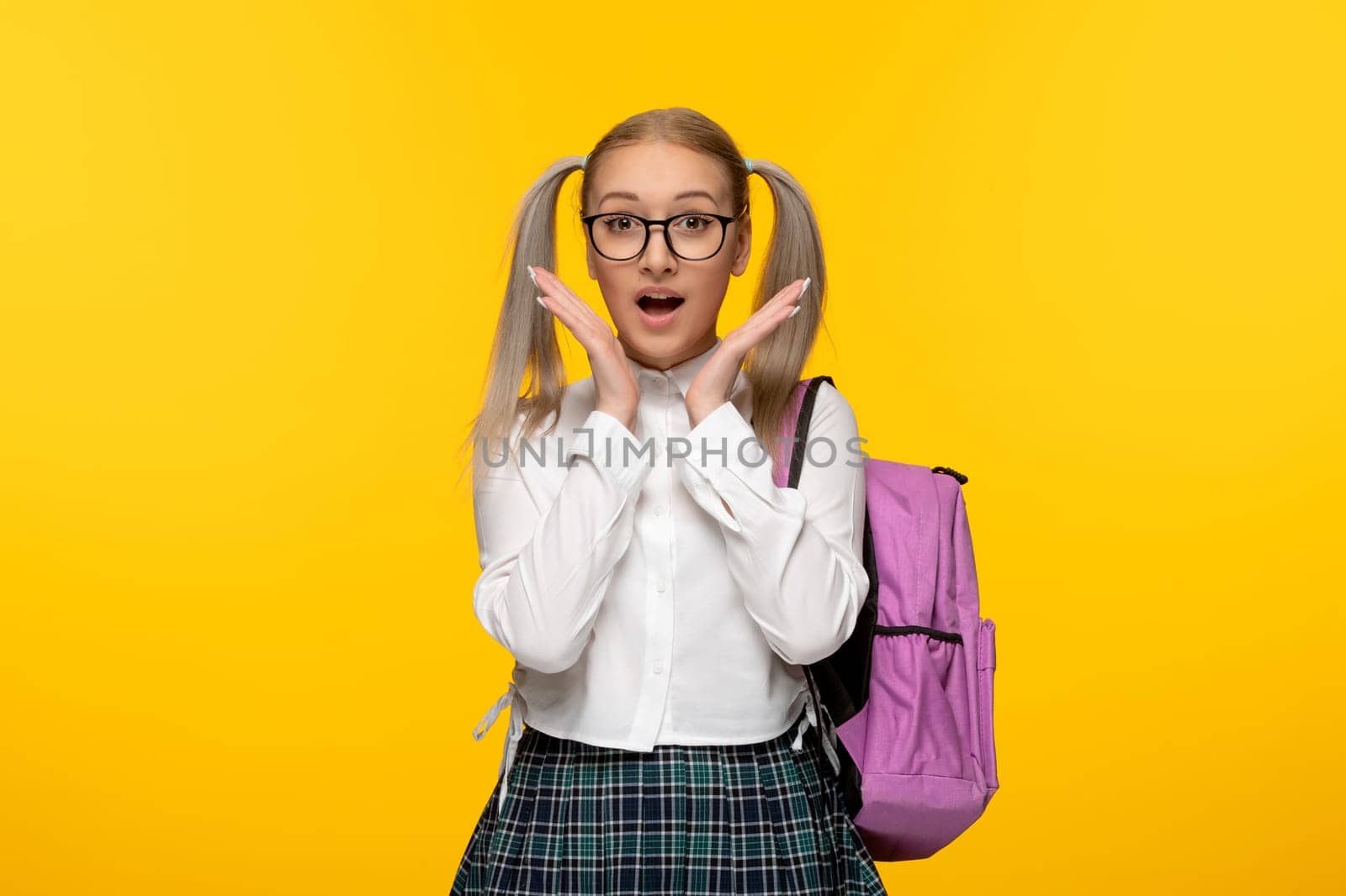 world book day surprised schoolgirl with ponytails hands under chin on yellow background
