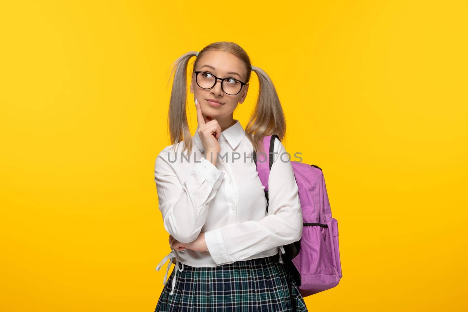 world book day thinking schoolgirl in glasses and pink backpack on yellow background
