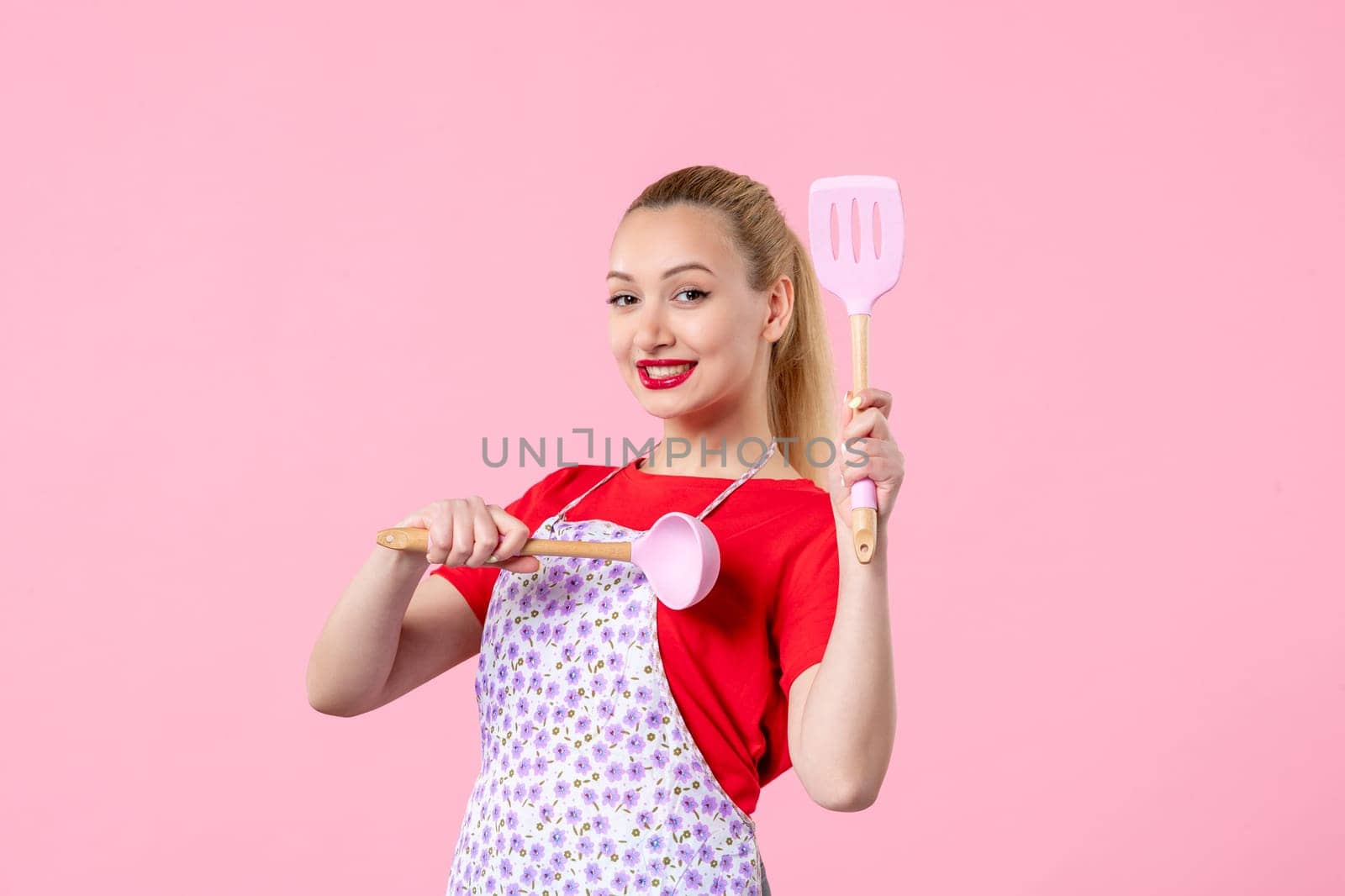 front view young pretty housewife in cape with spoons on pink background colors profession job uniform horizontal cooking worker