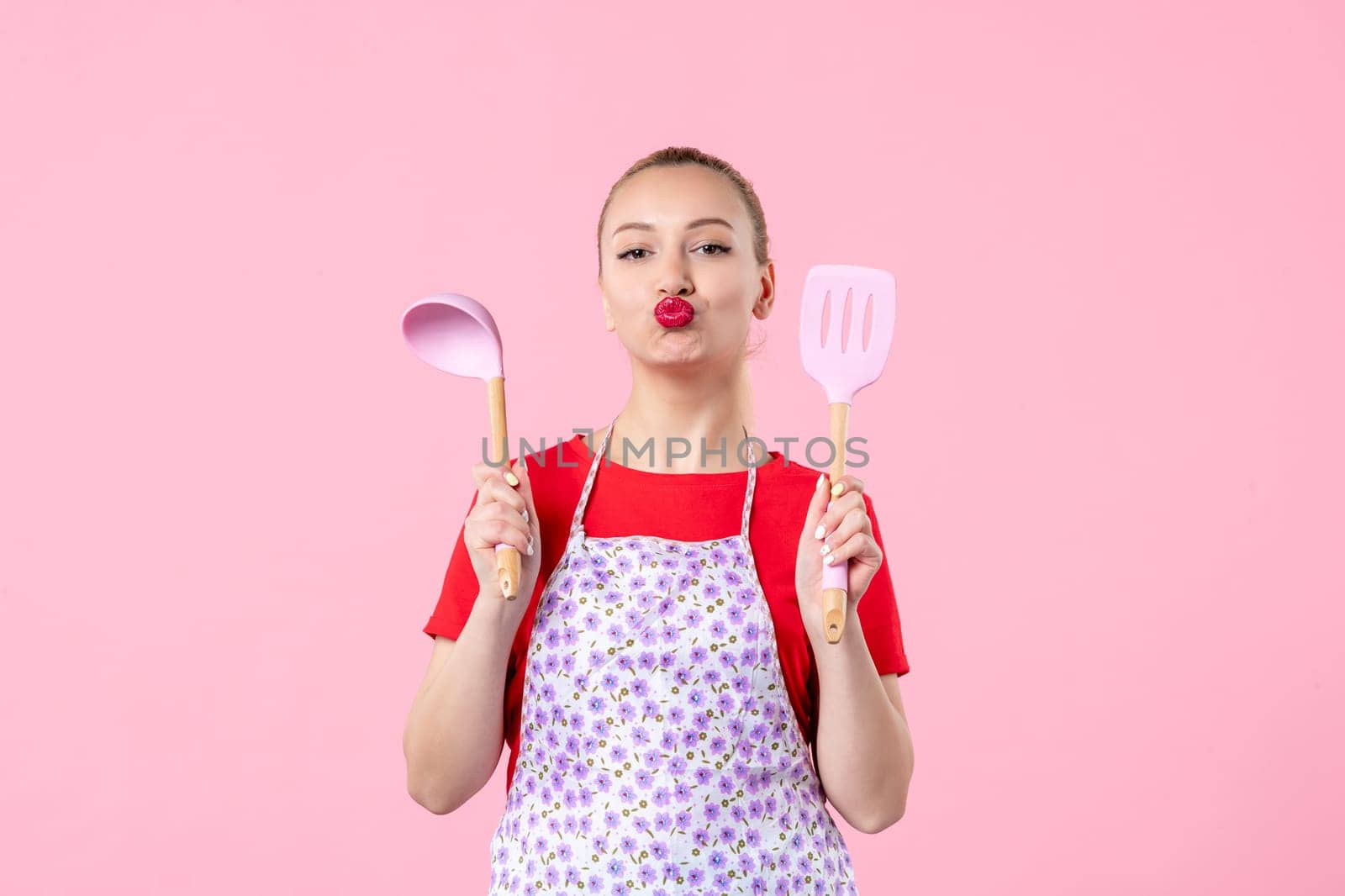front view young pretty housewife in cape with spoons on pink background profession cooking worker uniform job color