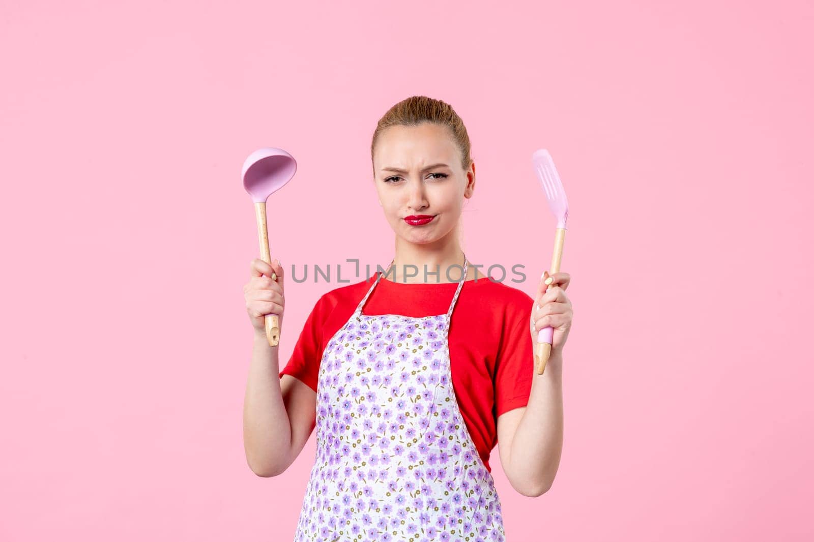 front view young pretty housewife in cape with spoons on pink background uniform duty job profession cooking wife horizontal occupation by Kamran