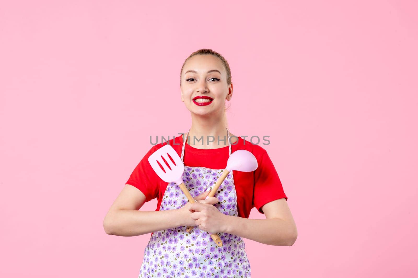 front view young pretty housewife in cape with spoons on pink background uniform job profession cooking worker wife duty occupation