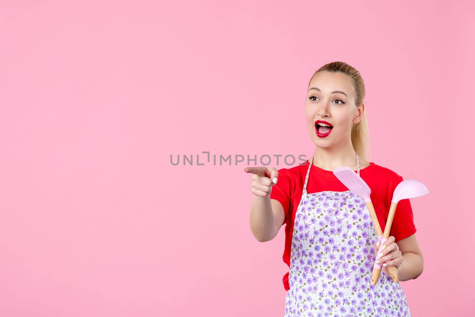 front view young housewife in cape holding spoons and interacting with someone on pink background profession cutlery occupation duty uniform job worker wife