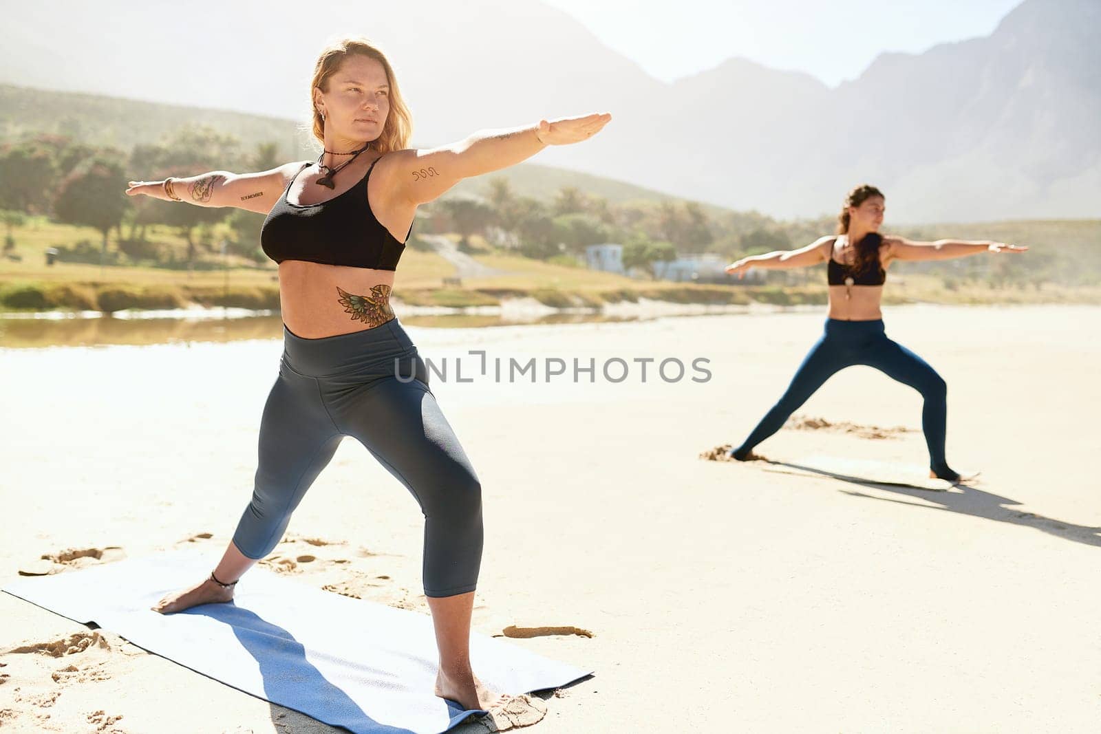 Yoga can help you discover the bodys hidden potential. two young woman practising yoga on the beach. by YuriArcurs