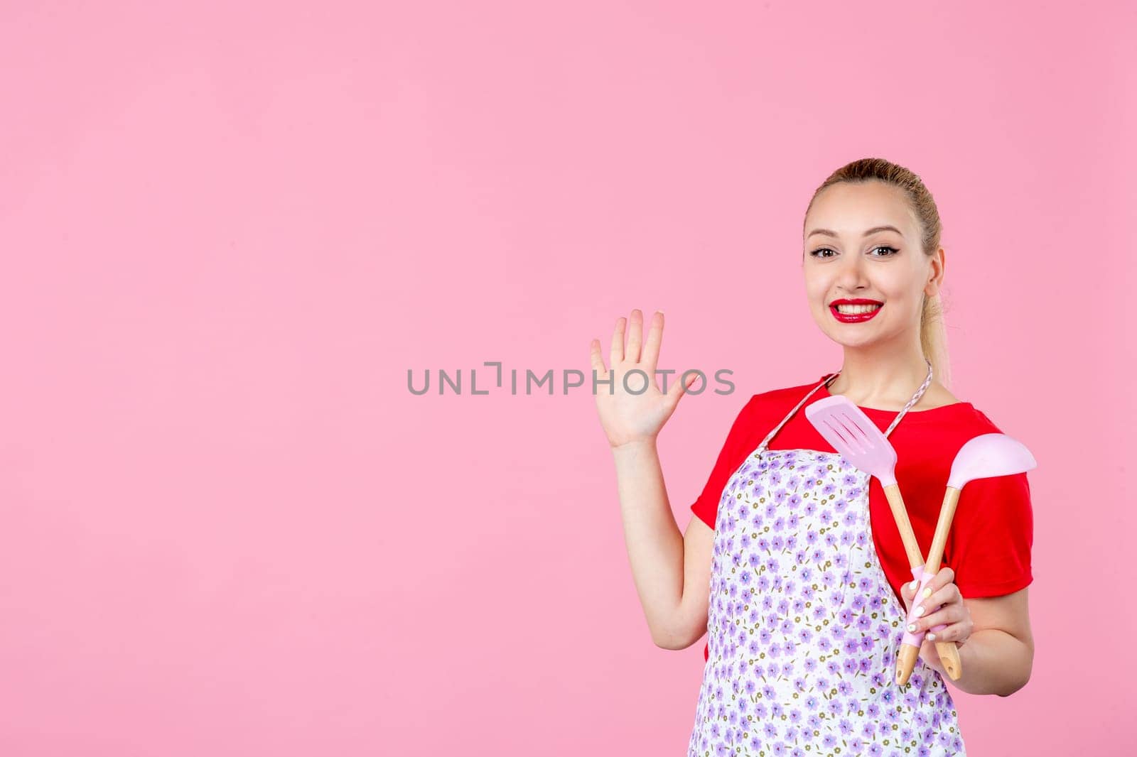 front view young housewife in cape holding spoons on pink background horizontal profession duty job worker wife uniform cutlery