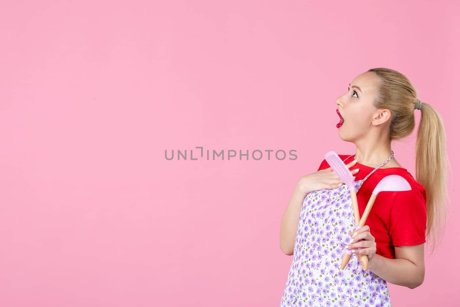 front view young housewife in cape holding spoons on pink background horizontal profession duty job worker wife uniform cutlery occupation