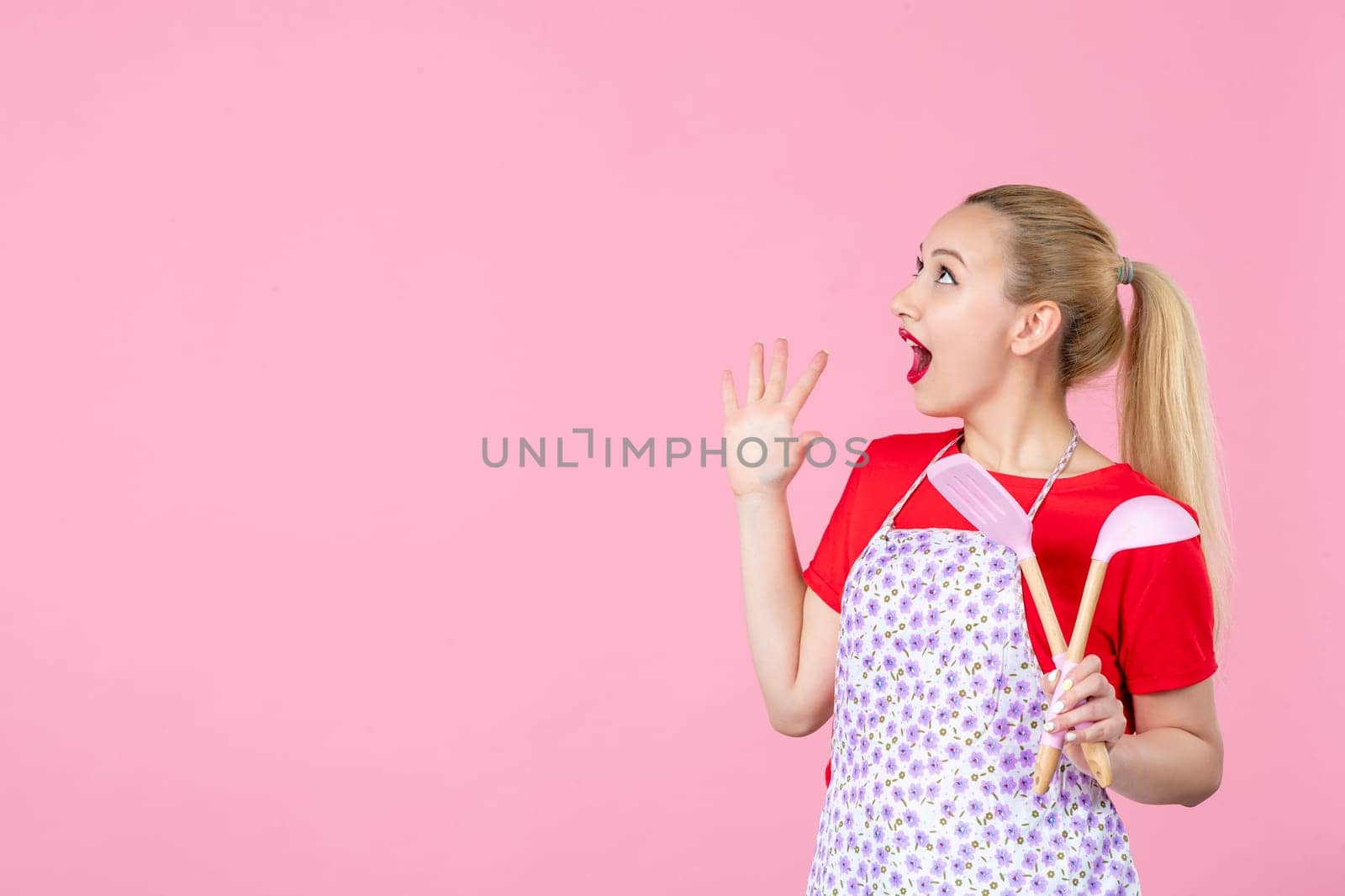 front view young housewife in cape holding spoons on pink background horizontal profession duty job worker wife uniform occupation