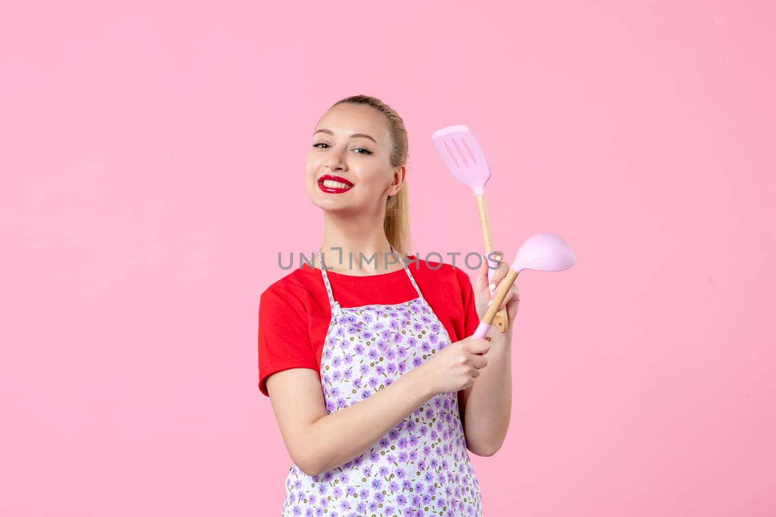 front view young housewife in cape holding spoons on pink background horizontal uniform duty occupation profession cutlery job worker by Kamran