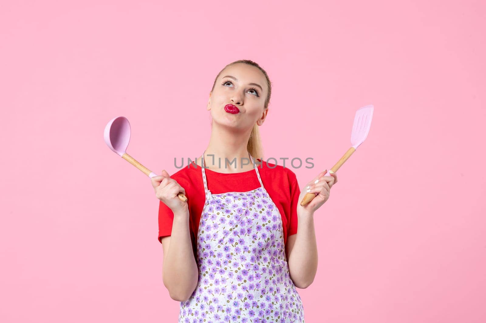 front view young housewife in cape holding spoons on pink background horizontal uniform duty profession cutlery job wife worker occupation