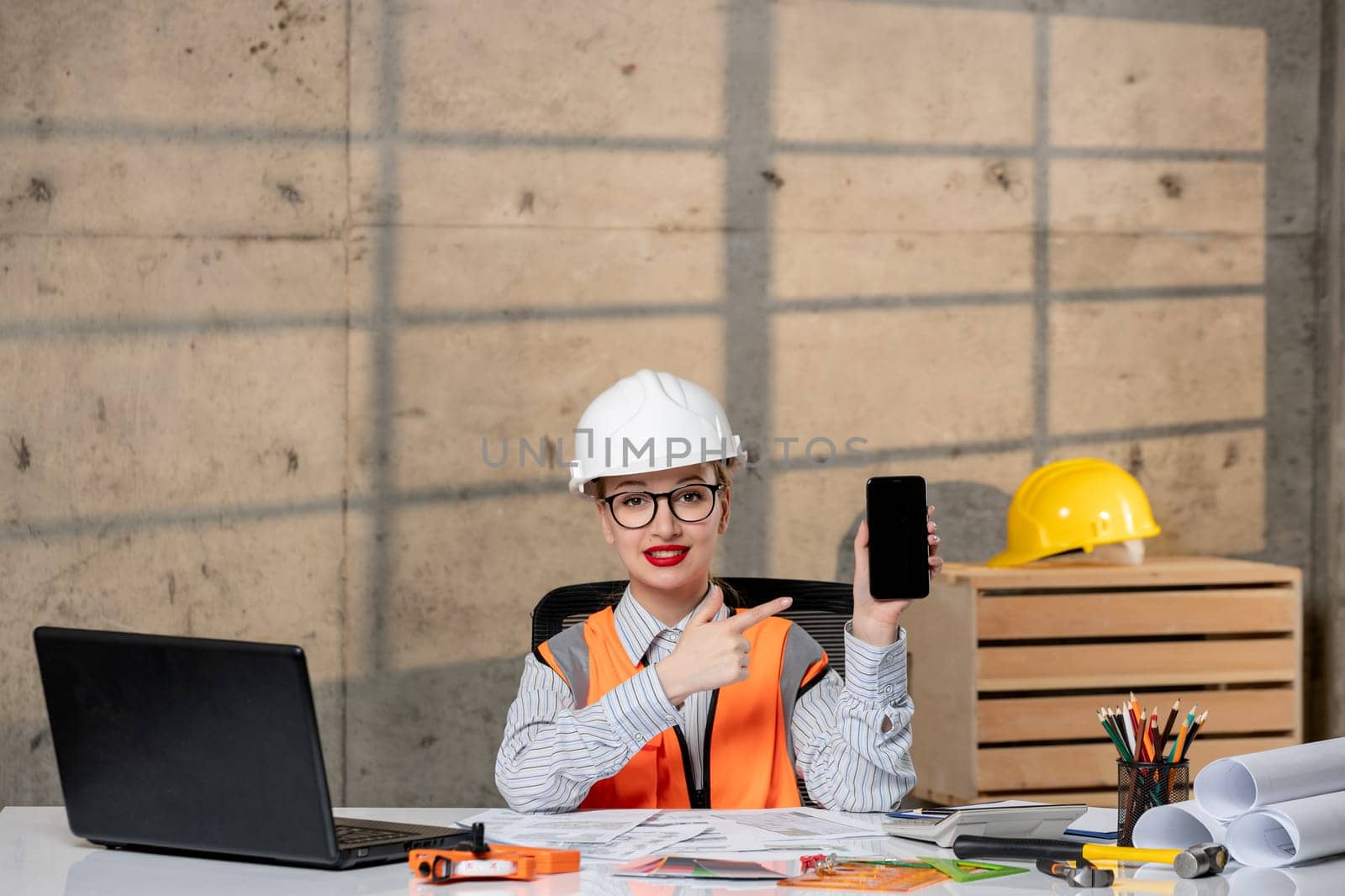 engineer blonde young cute smart girl civil worker in helmet and vest with phone by Kamran