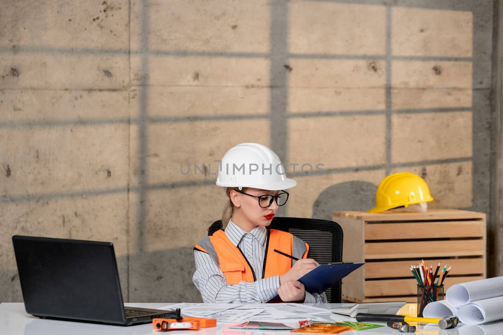 engineer cute young blonde smart girl civil worker in helmet and vest writing