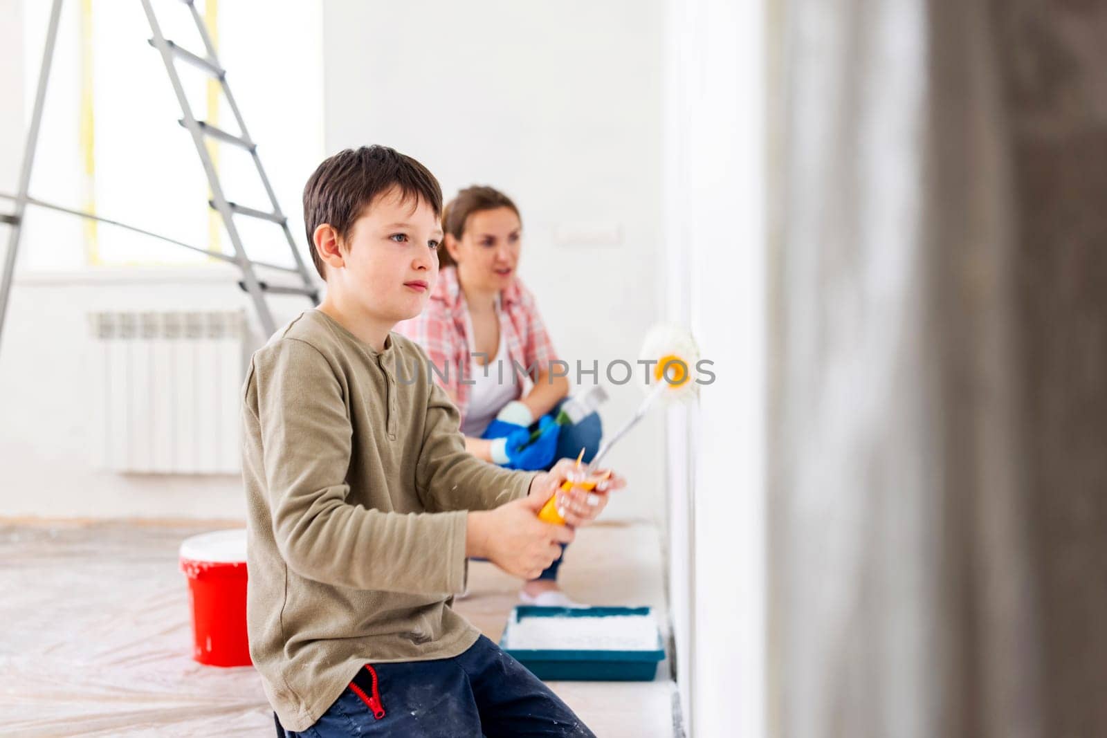 Happy family mother and child son paint the wall with paint using roller and brush. Repair in the apartment