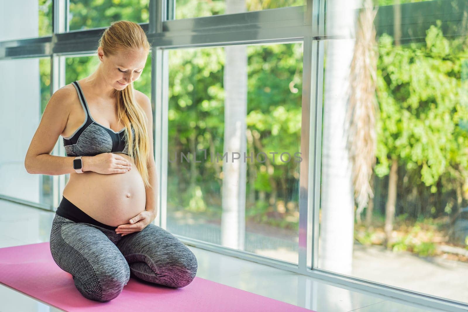 Young pregnant woman doing yoga exercises and meditating at home or yoga studio. Health care, mindfulness, relaxation and wellness concept.
