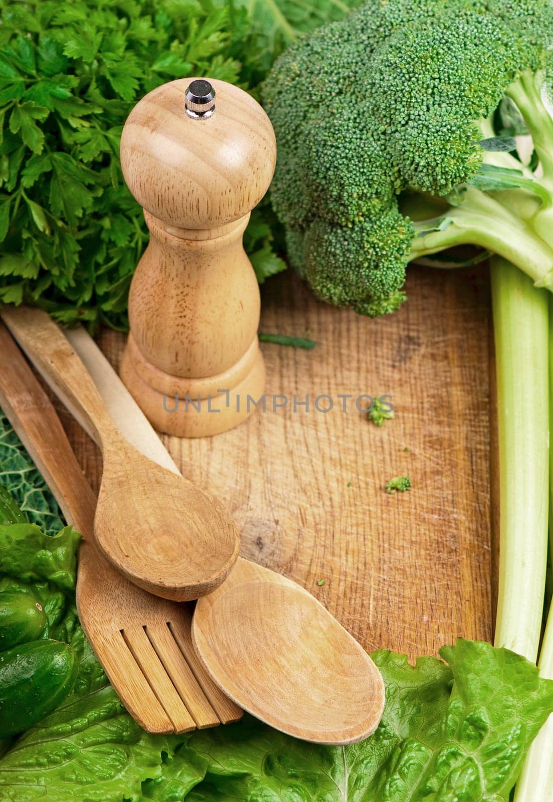 kitchen wooden utensils on table, surrounded by green vegetables. by aprilphoto