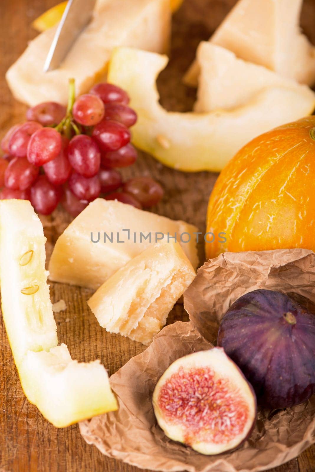 Cheese plate served with grapes, melon, figs, crackers, honey, nuts and white wine on a wooden table by aprilphoto
