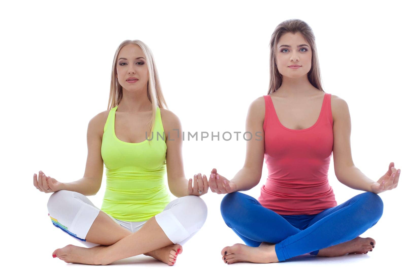 Pair of pretty young girls meditates in studio, isolated on white