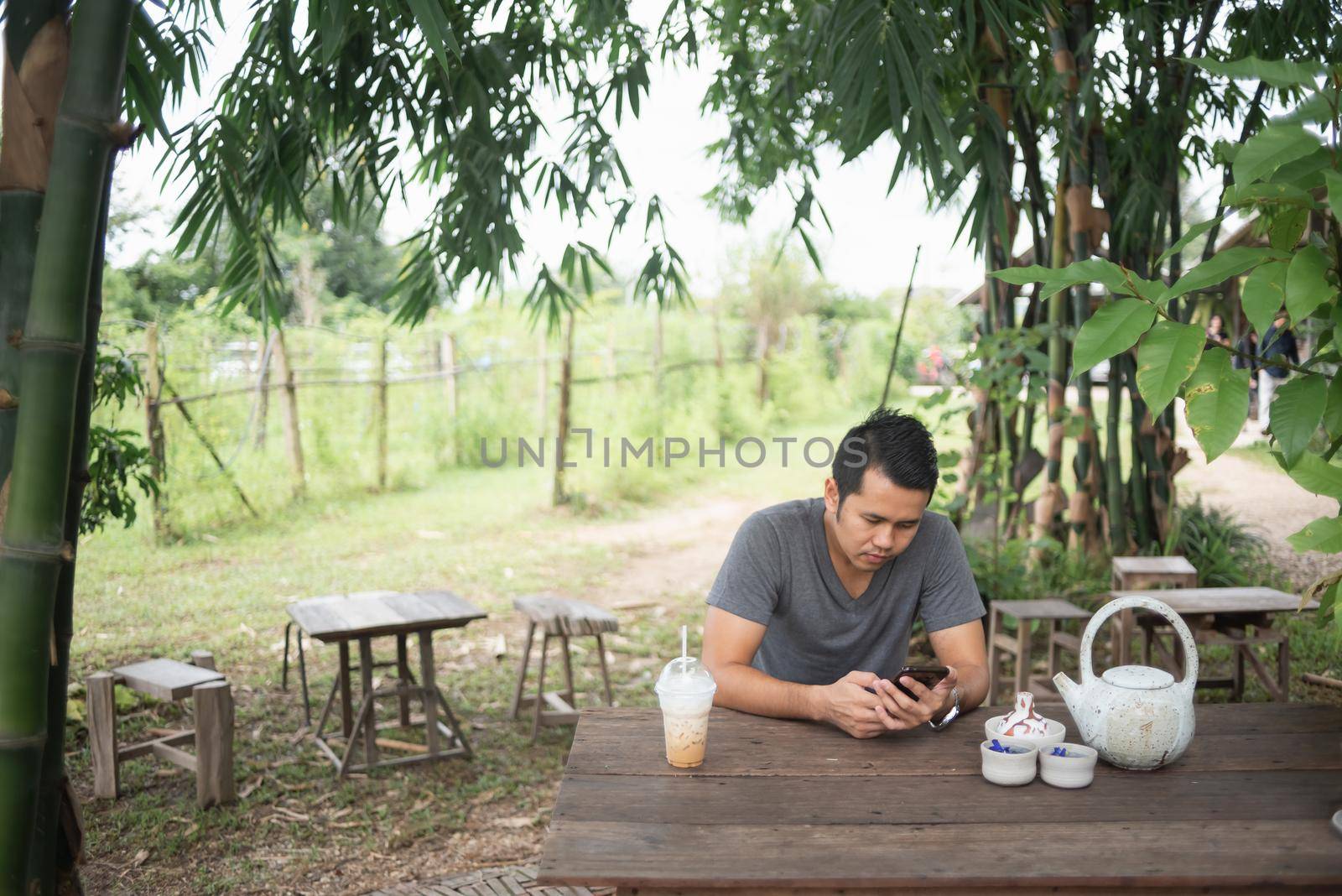 the man using mobile phone and drink ice coffee on wood table