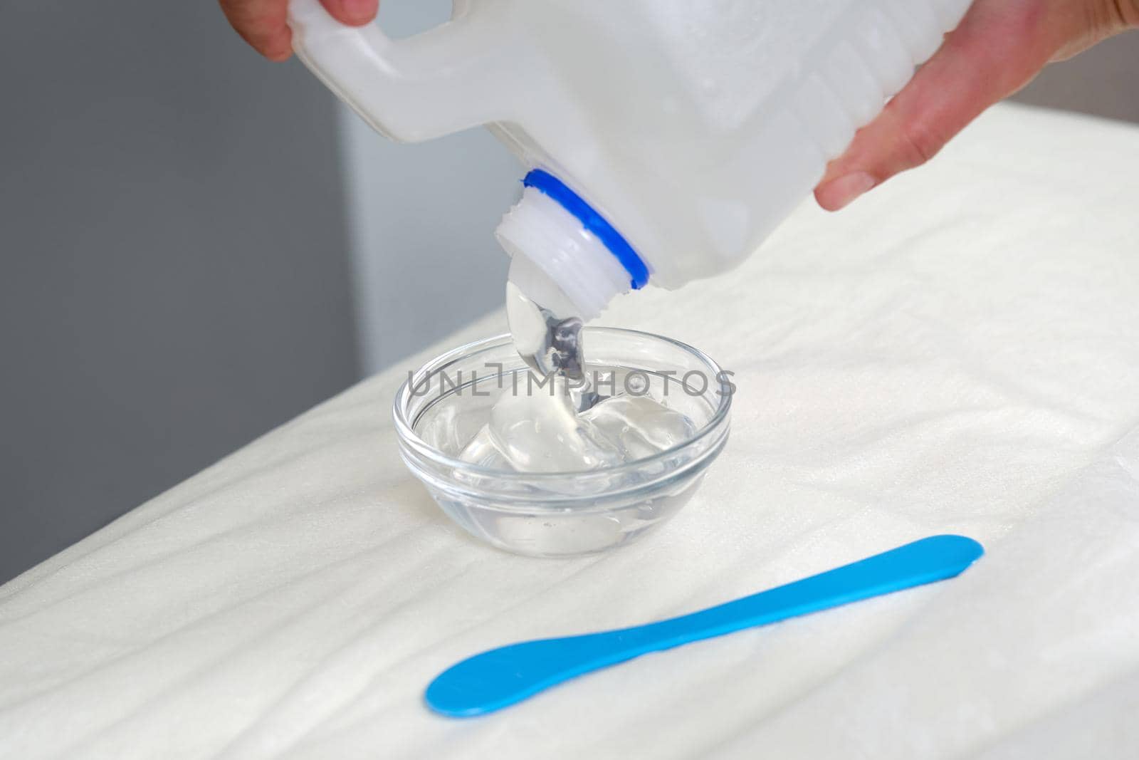 cosmetologist pooring transparent gel from a big bottle before beauty treatment