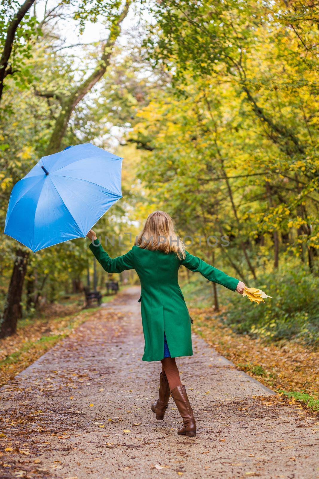 Woman holding umbrella and fall  leaves while jumping and  walking in the park.