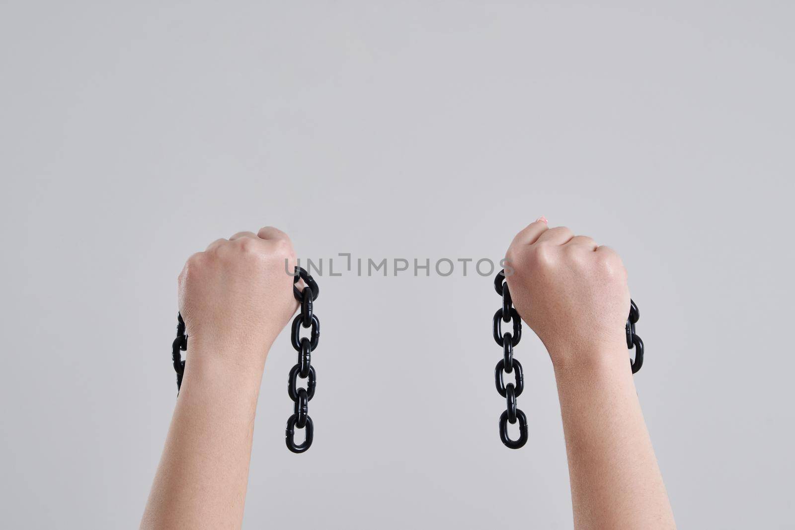 Female hands holding a broken metal chain over grey background