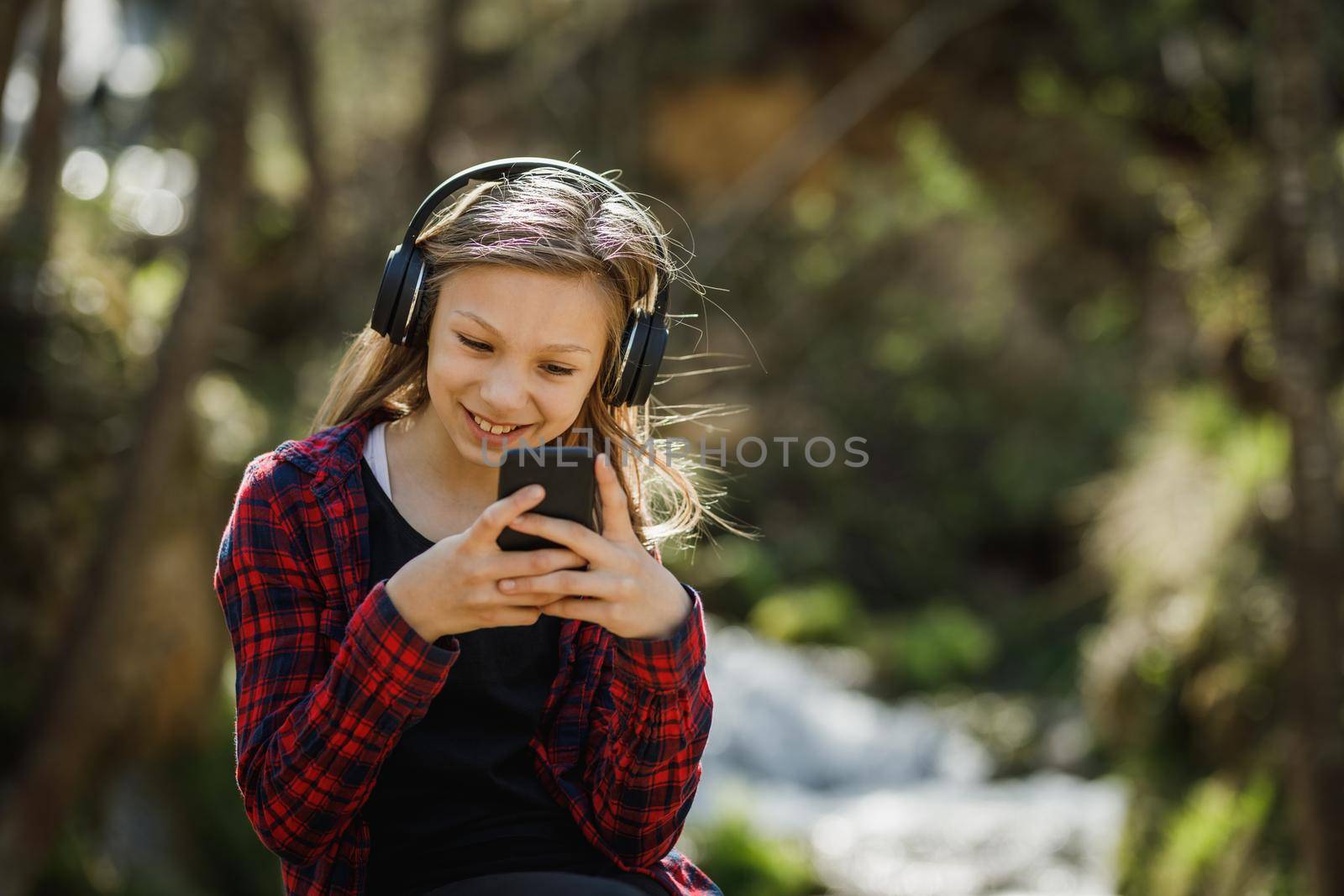 A smiling teenager girl using her smartphone while listening music in nature.