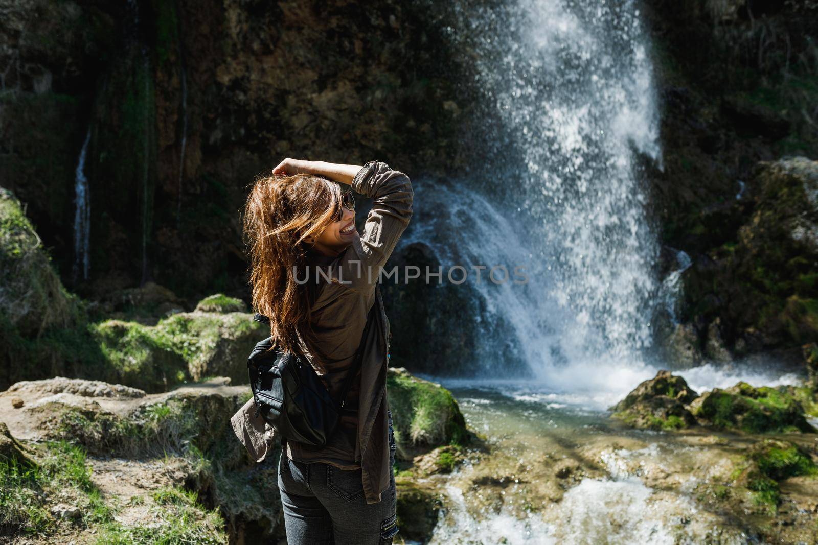 A smiling young woman enjoying the view of the beautiful waterfall.