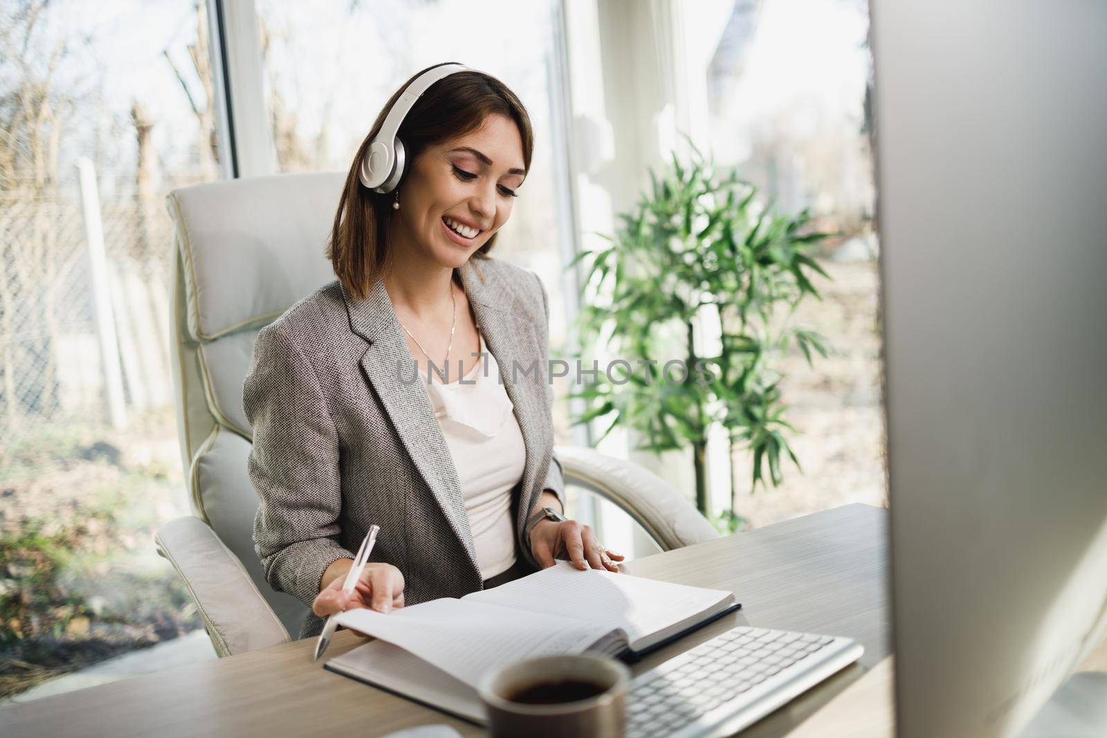 An attractive young woman with headphones working on computer at home office.