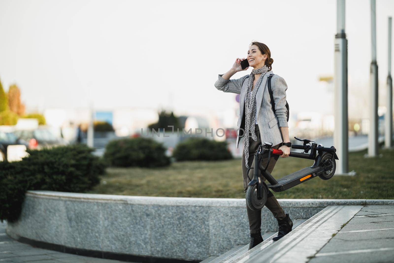 Shot of a young businesswoman using a smartphone while traveling with an electric scooter through the city.