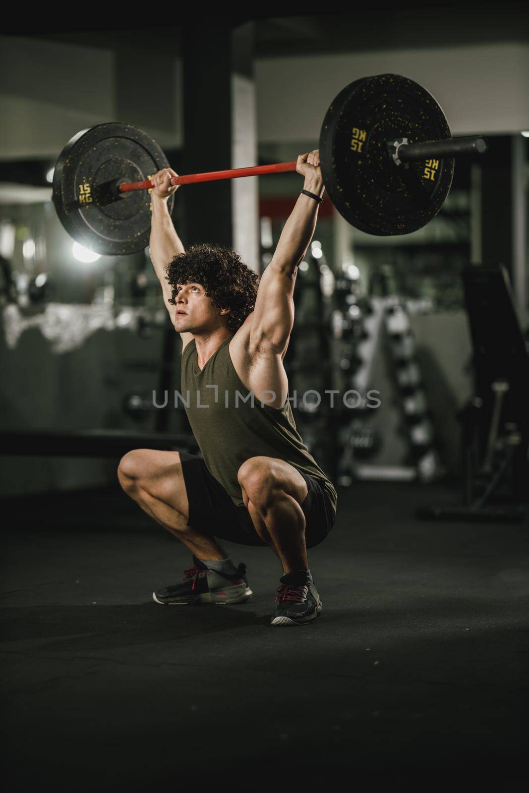 A young muscular man is doing hard training with barbell at the gym.