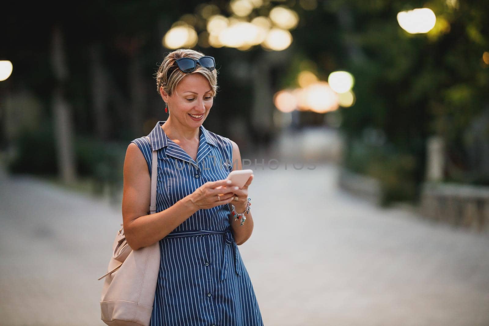 Mature attractive woman using a smartphone and walking at night while enjoying a summer vacation.