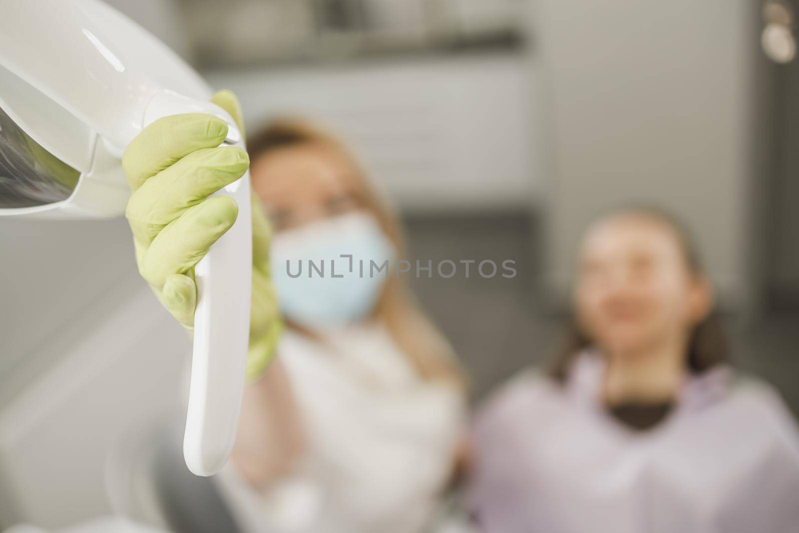 Close-up of an unrecognisable dentist holding dental lamp while having a consultation with patient in an office .