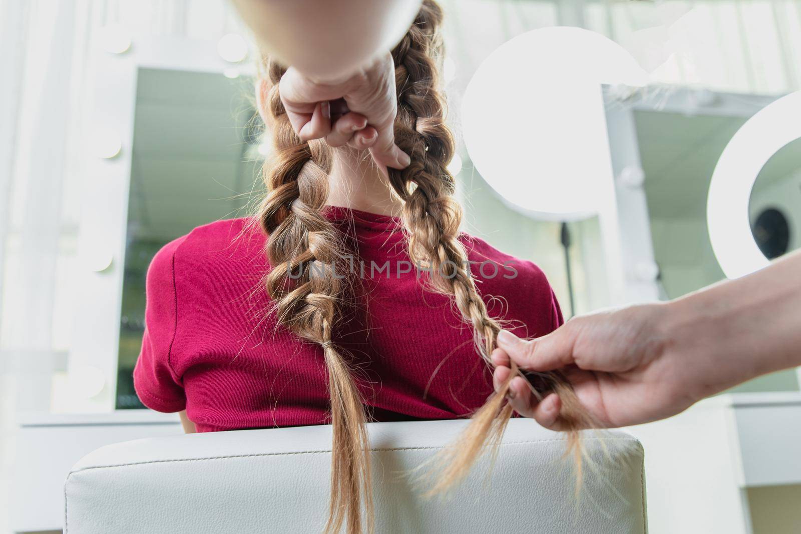 Hairdresser weaves a braid to a preteen blond girl