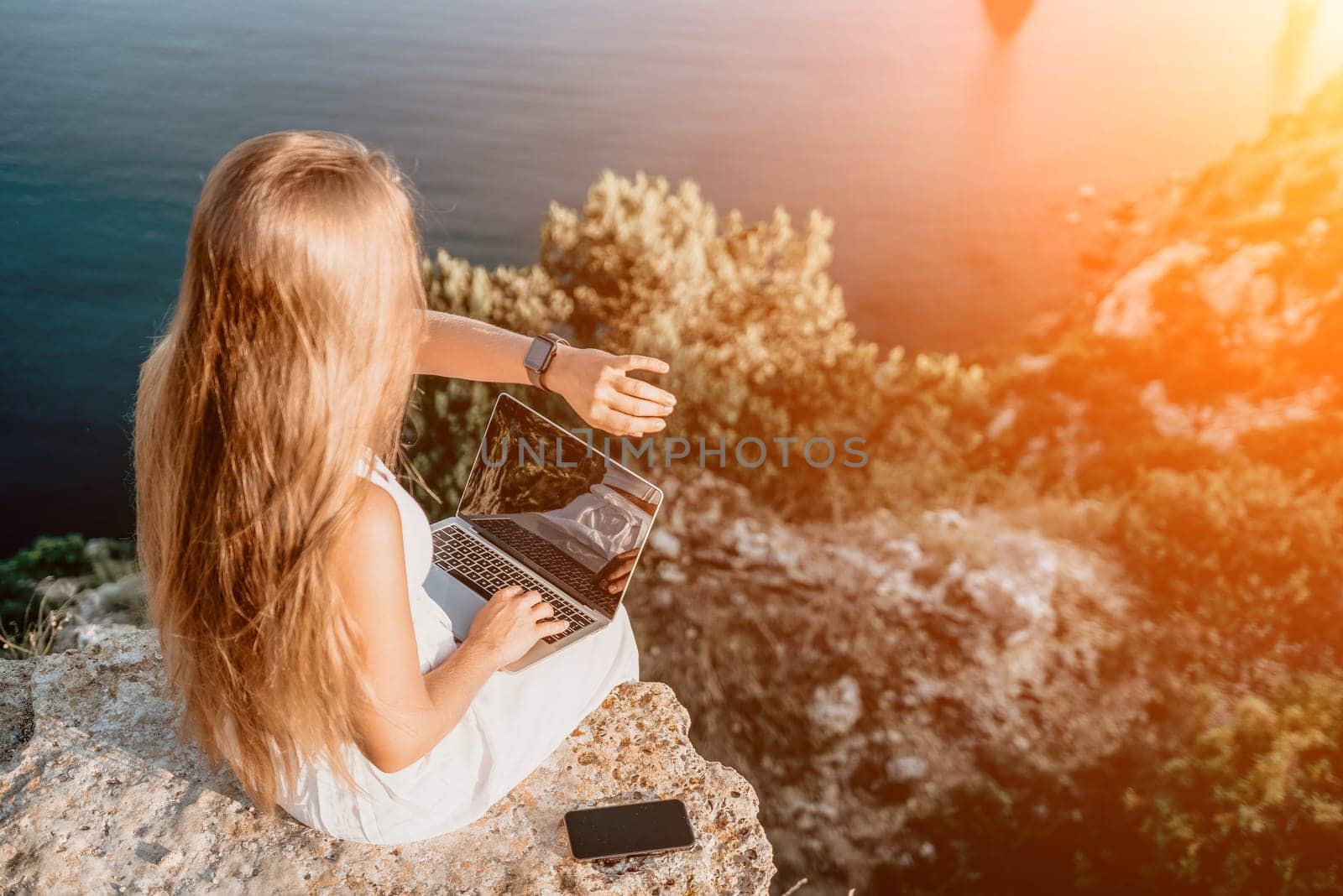 Successful business woman in yellow hat working on laptop by the sea. Pretty lady typing on computer at summer day outdoors. Freelance, travel and holidays concept.