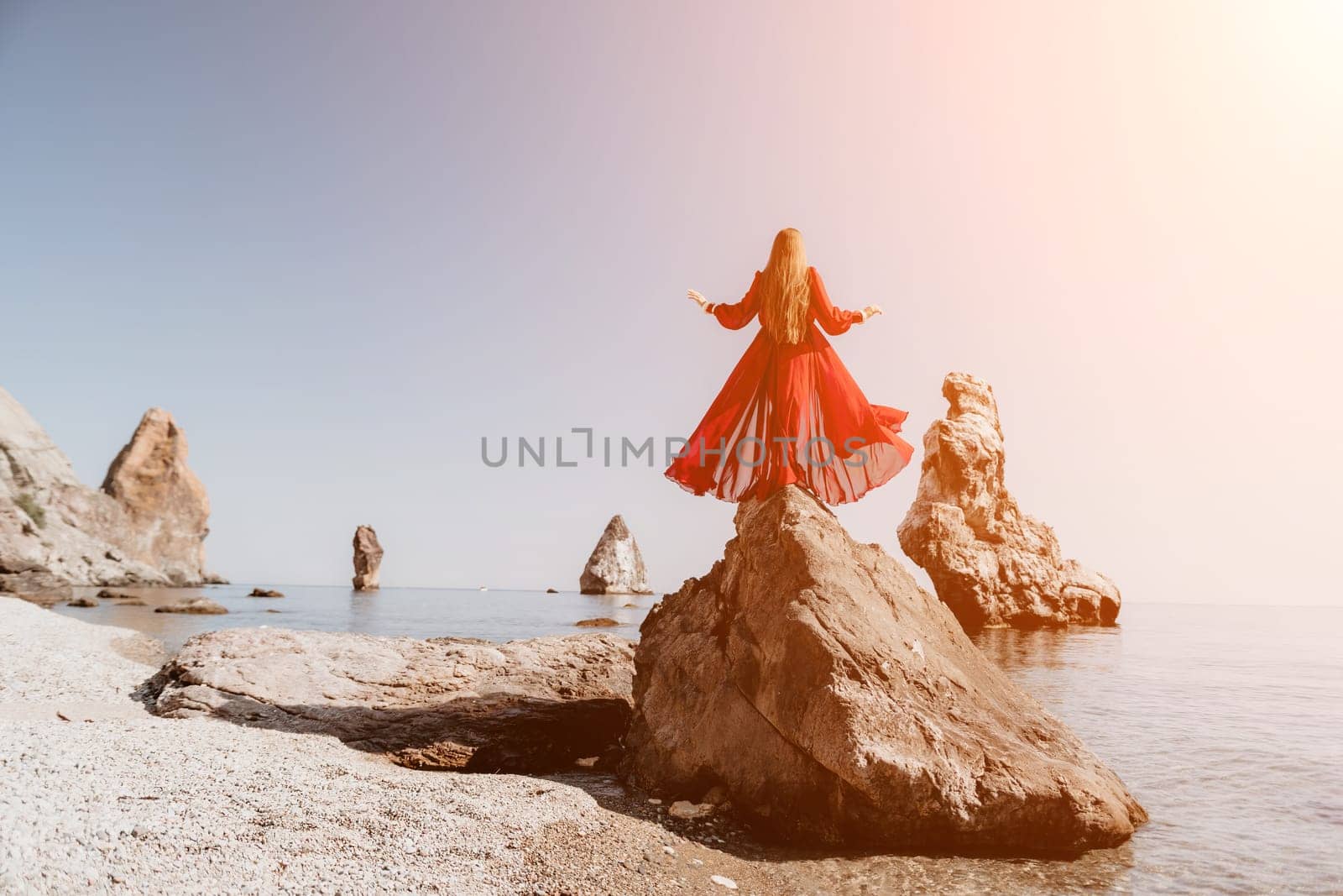 Woman travel sea. Young Happy woman in a long red dress posing on a beach near the sea on background of volcanic rocks, like in Iceland, sharing travel adventure journey by panophotograph