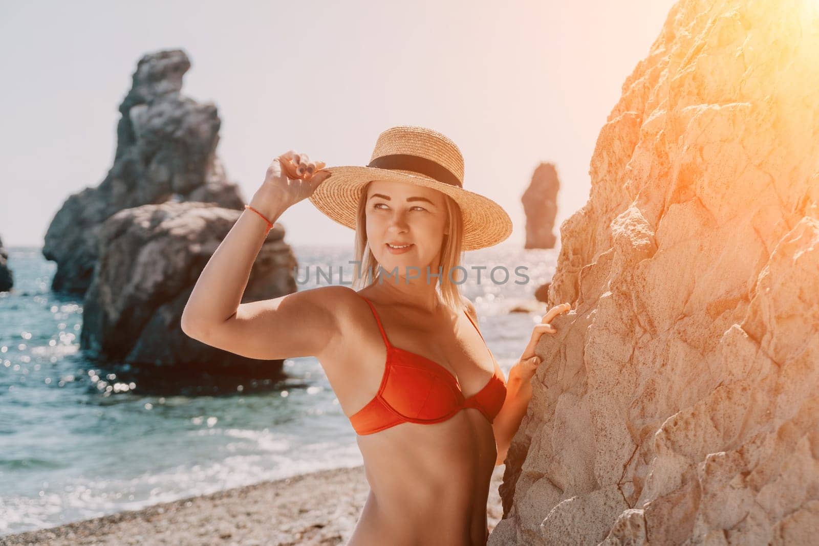 Woman travel sea. Young Happy woman in a long red dress posing on a beach near the sea on background of volcanic rocks, like in Iceland, sharing travel adventure journey