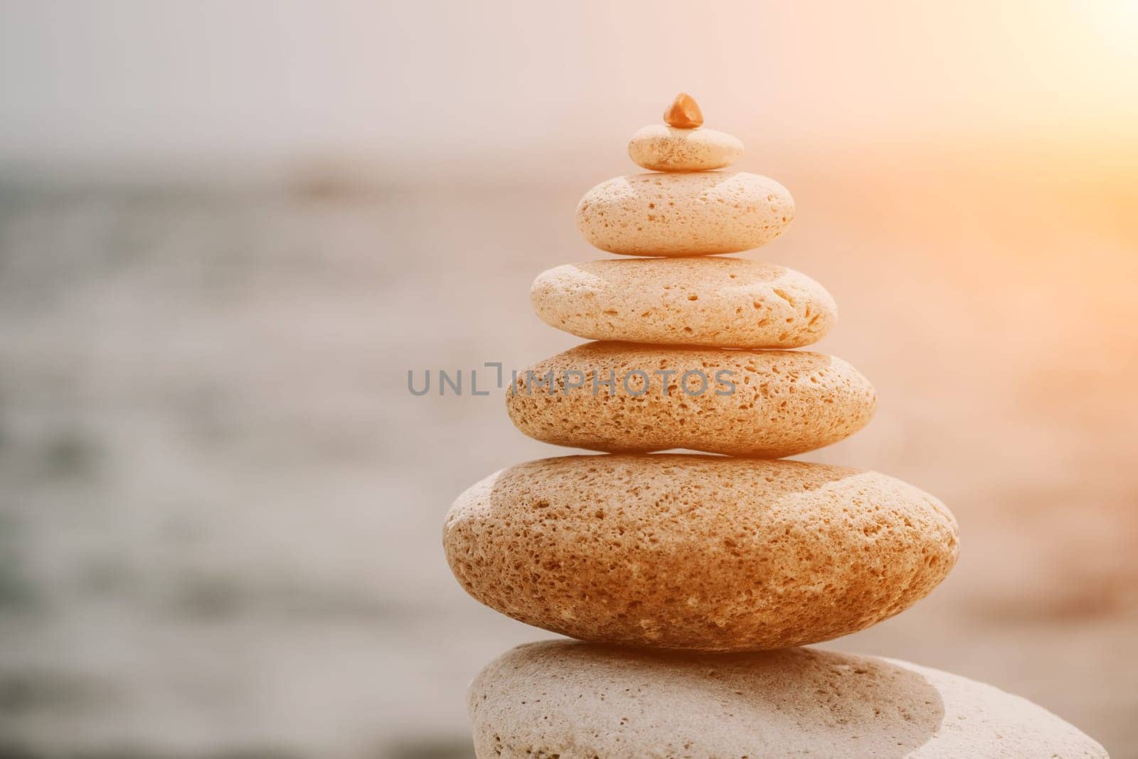 Pyramid stones on the seashore with warm sunset on the sea background. Happy holidays. Pebble beach, calm sea, travel destination. Concept of happy vacation on the sea, meditation, spa, calmness.