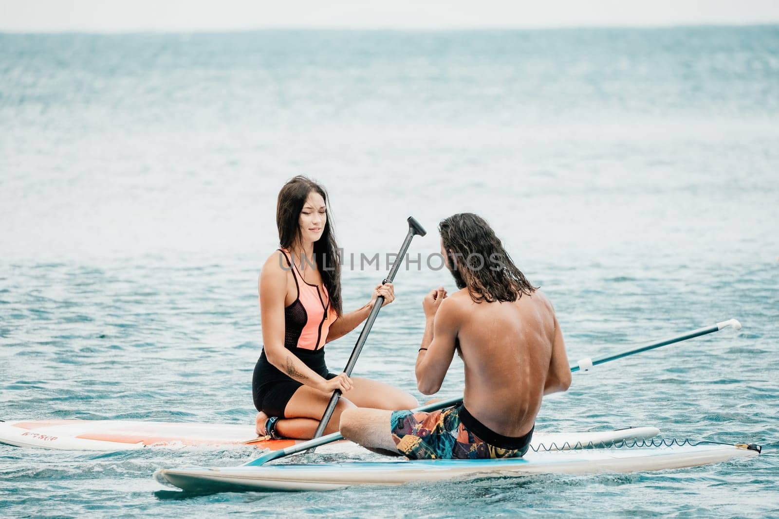 Sea woman and man on sup. Silhouette of happy young woman and man, surfing on SUP board, confident paddling through water surface. Idyllic sunset. Active lifestyle at sea or river. by panophotograph