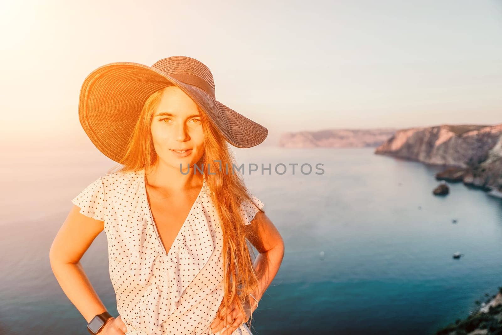 Portrait of happy young woman wearing summer black hat with large brim at beach on sunset. Closeup face of attractive girl with black straw hat. Happy young woman smiling and looking at camera at sea