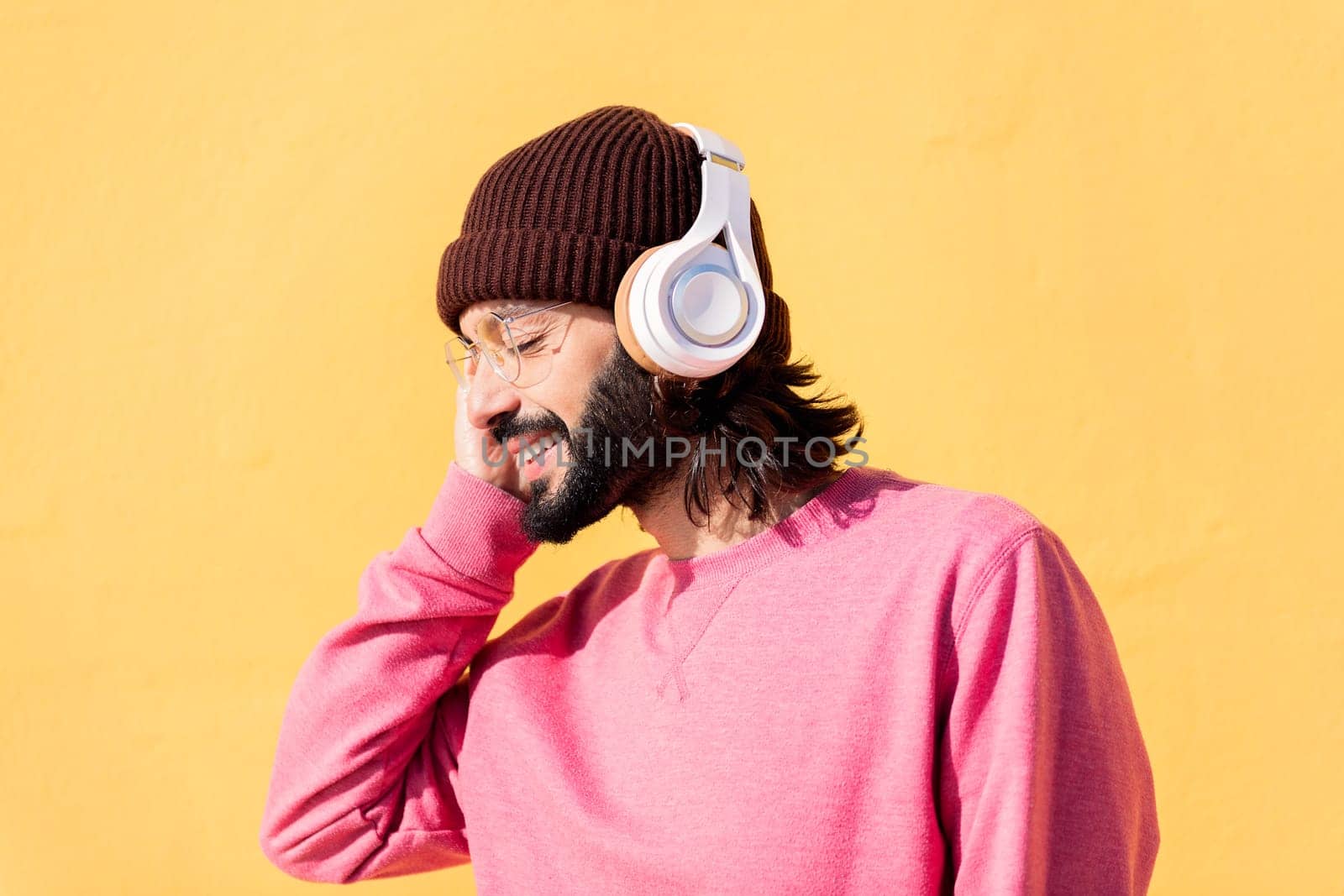 young man enjoying happy the music in his headphones with a yellow wall in the background, concept of rhythm and positive people, copy space for text