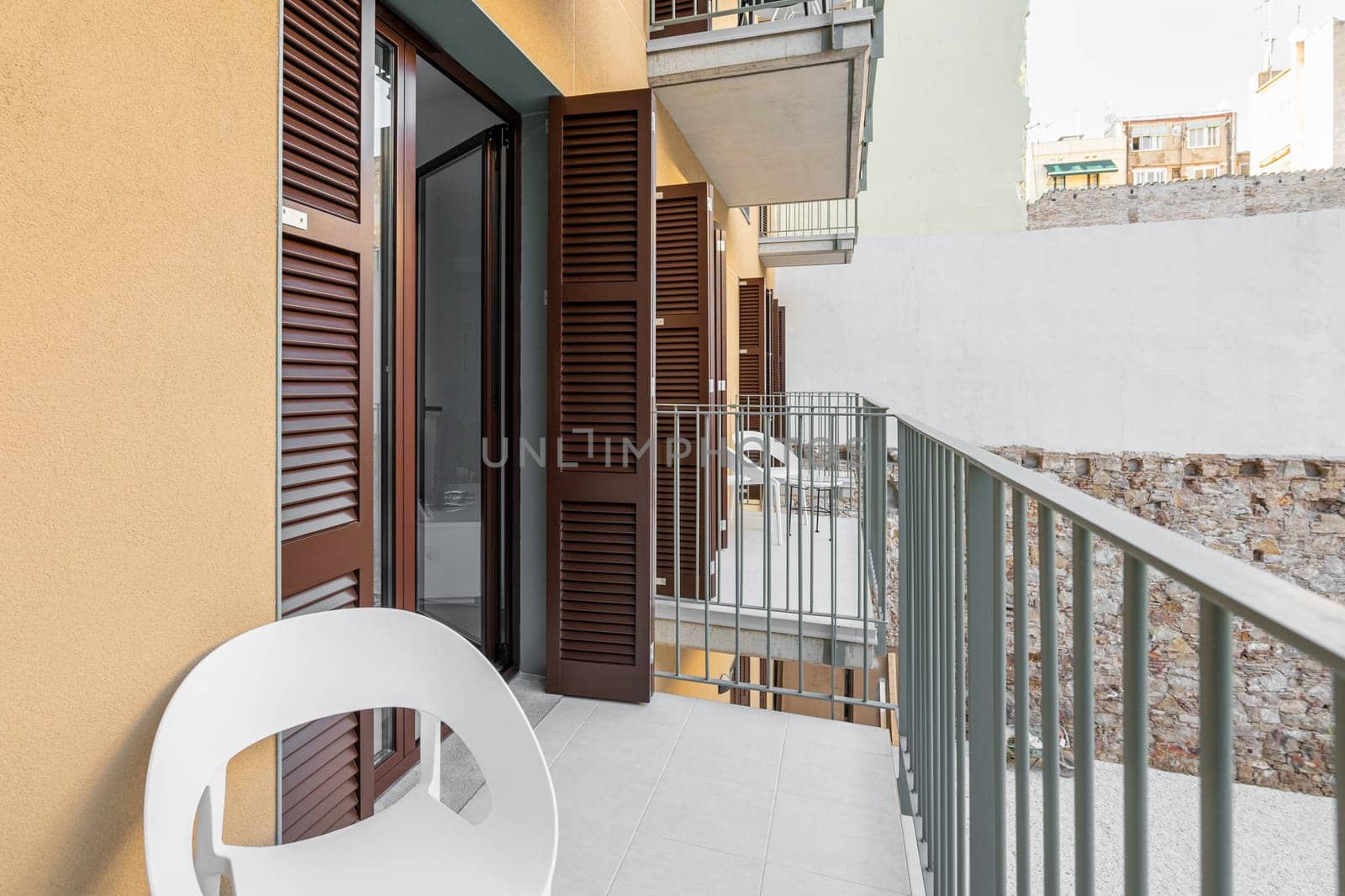 Exit from the apartment on an unglazed balcony with a chair and a view of the courtyard and other balconies and open doors of the houses. Leisure and fresh air concept.