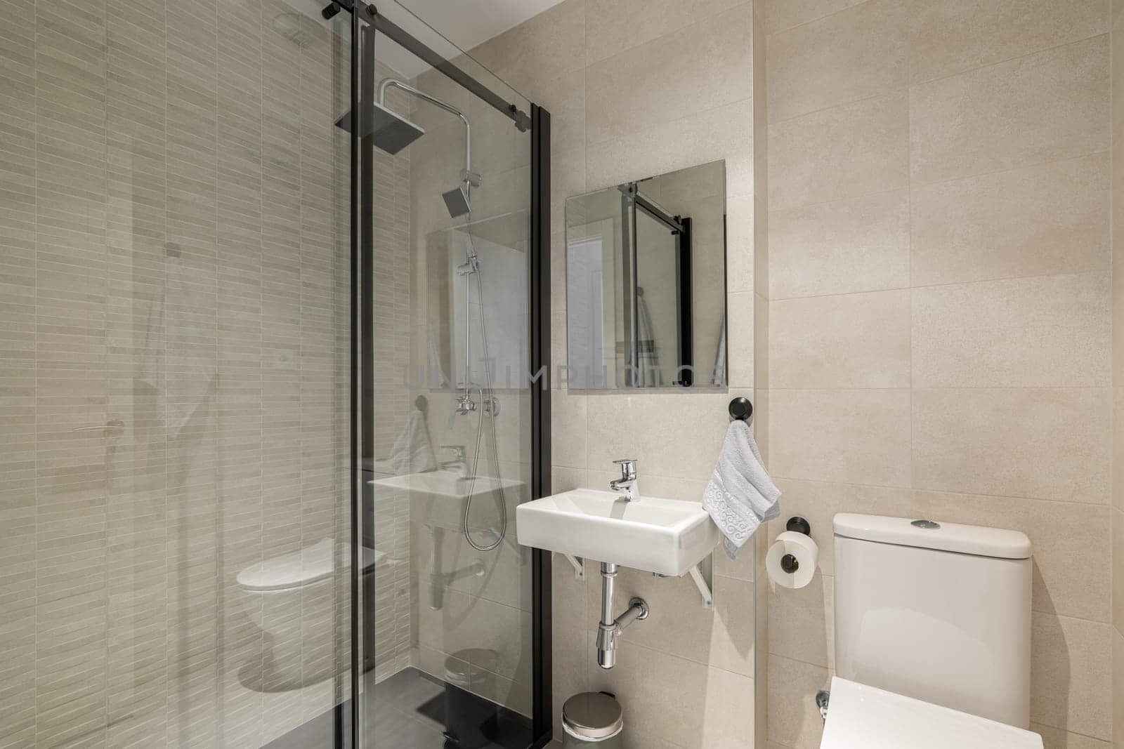 Stylish comfortable bathroom with a glass-enclosed shower, toilet and sink and a mirror in light colors with beige tiles. The concept of a comfortable hotel room with a modern interior.