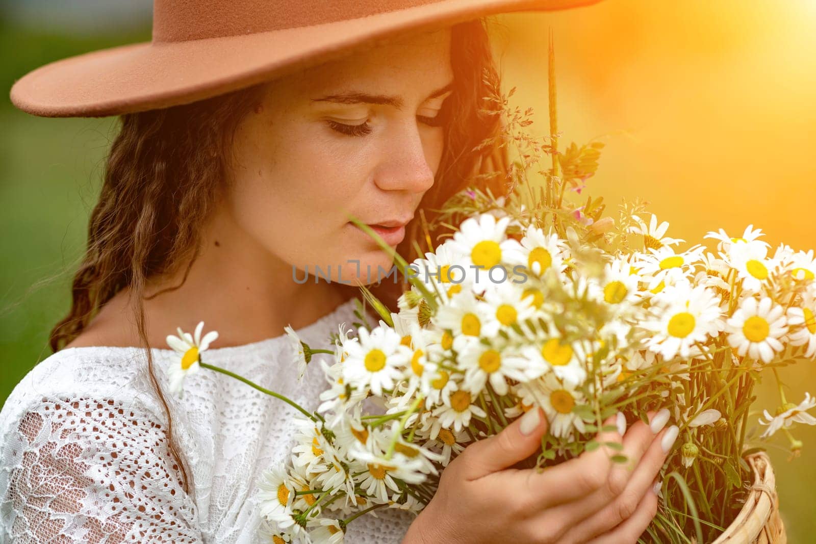 A middle-aged woman in a white dress and brown hat holds a large bouquet of daisies in her hands. Wildflowers for congratulations by Matiunina