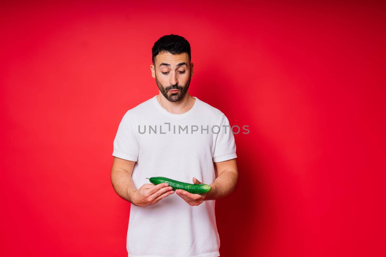 Male hand holding cucumber on red background, space for text by Zelenin