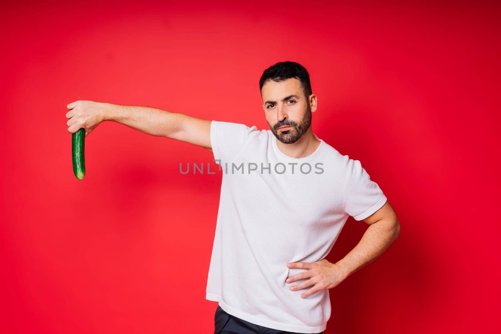 Male hand holding cucumber on red background, space for text by Zelenin