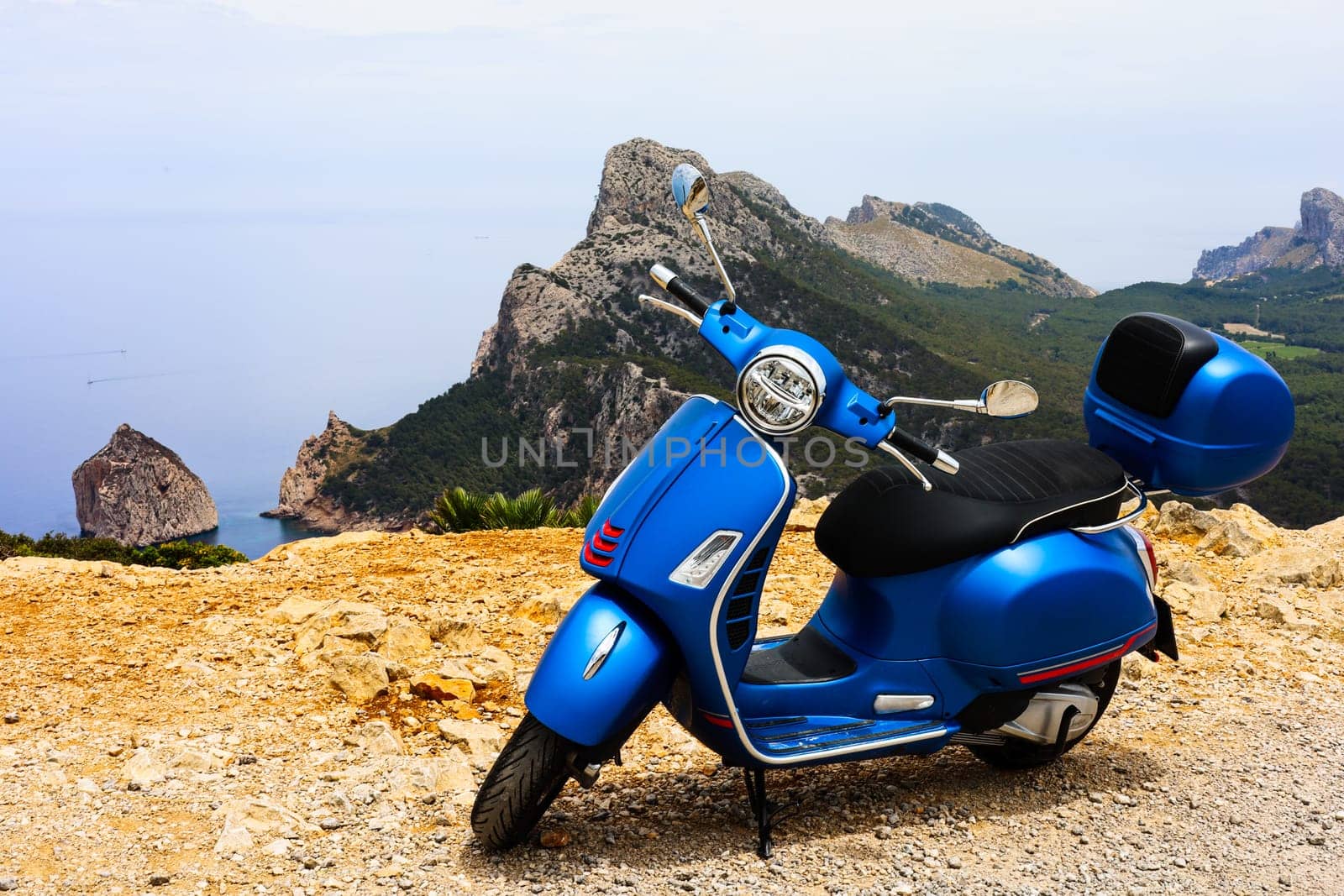 Blue motor scooter on coastal road with sea and rocks in background. High quality photo